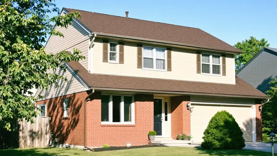 Two-story house with a dark brown architectural shingle roof over red brick, tan siding and cream trim