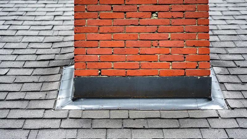Brick chimney with step flashing under shingles and counter flashing set in a sealed mortar reglet