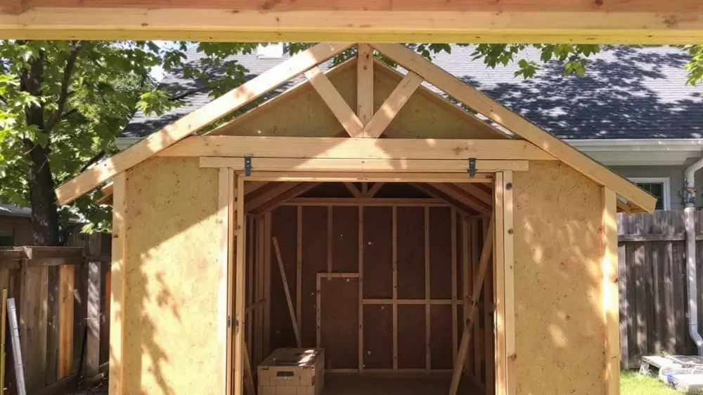 Backyard shed framing with 2x4 gable rafters meeting at a ridge board above horizontal rafter ties