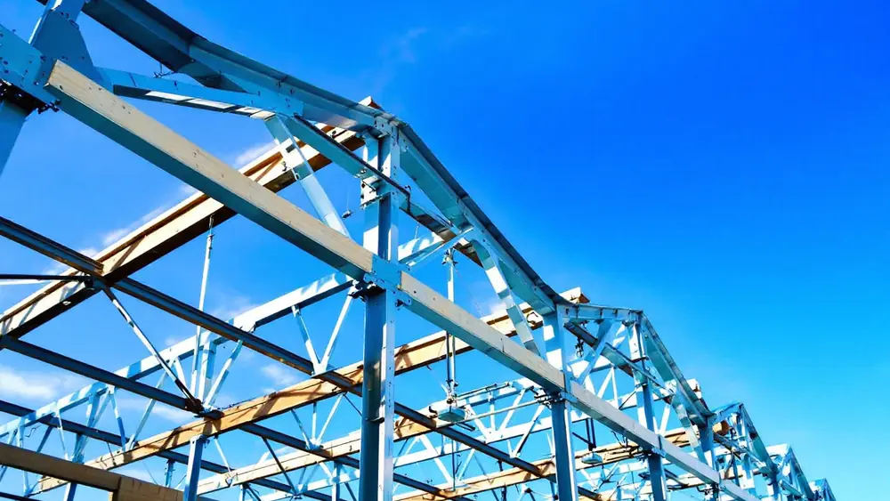 Black welded angle-iron steel gable trusses bolted to wood posts on a pole barn frame, with wood purlins in steel cups