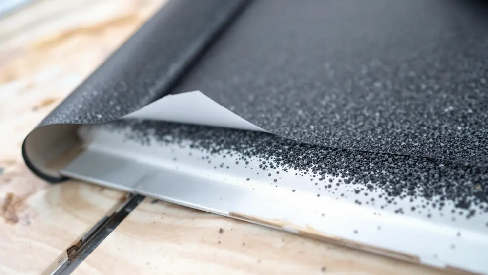 Granulated self-adhered ice and water barrier roll unrolled on a plywood roof deck over a metal drip edge
